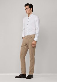 Witte button-up shirt met bruine knopen, gecombineerd met khaki broeken en donkerbruine schoenen. Eenvoudig ontwerp, getailleerde silhouet, soepele stoftextuur.
