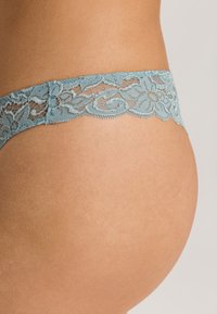 Spitzen-Tanga in Hellblau mit floralem Muster, ausgestattet mit gewellten Kanten. Weicher Stoff, der für Komfort sorgt, mit einem niedrig geschnittenen Design.