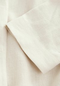 Linnedug i en lys beige farve med en blød, struktureret overflade. Har en ombukket kant med enkle syningsdetaljer.