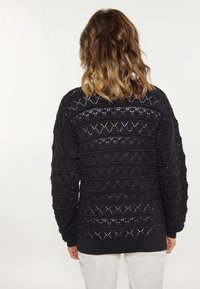 Pulover negru tricotat, cu modele cu deschidere, benzi texturate și tiv cu dungi. Mâneci lungi cu o croială relaxată.