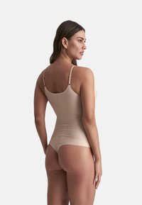 Beige shapewear bodysuit met verstelbare banden, zachte stof, figuurvormend ontwerp en een naadloze achterkant voor een gestroomlijnd silhouet.