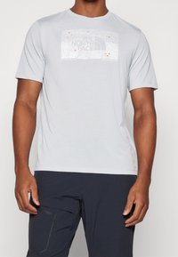 Ljusgrå kortärmad t-shirt med en textured karta och logo. Mjuk tyg med en avslappnad passform, ihop med mörka byxor.