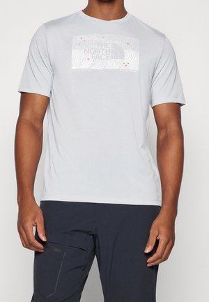 Lys grå kortærmet t-shirt med et tekstureret kortdesign og logo. Blødt stof med en afslappet pasform, kombineret med mørke bukser.