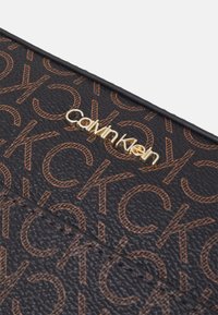 Czarny portfel z fakturowanej skóry, ozdobiony wytłoczonym pomarańczowym wzorem monogramu Calvin Klein oraz złotym akcentem z logo.