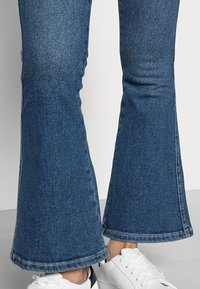 Uppsköljda blå jeans i denim, med rå kant och smal passform vid låren, kombinerade med vita sneakers.