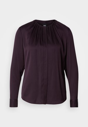 Dark purple long-sleeve blouse in smooth fabric with a round neckline, gathered detailing, and button closure at the front.