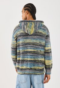 Hooded pulover iz mehkega materiala; vsebuje valovito vzorčenje modrih, sivih in rumenih odtenkov. Ohlapen kroj z rebrastimi manšetami in robom.
