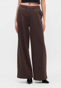 Φαρδιά, σκούρα καφέ φόρμα με ελαστική μέση και μαλακή υφή, συνδυασμένη με μαύρες γόβες με μυτερή μύτη.