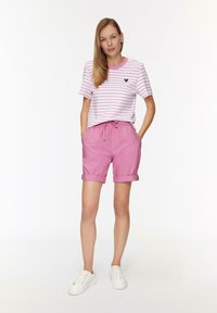 T-shirt rayé rose et blanc avec un col rond et un logo ; short rose avec une taille élastique et des revers roulés ; baskets blanches.