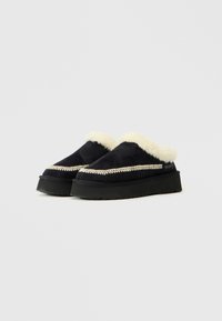 Melni slip-on apavi ar pūkainu baltu šerlinga oderi, ar dekoratīvo šuvju un biezām melnām gumijas zolēm.