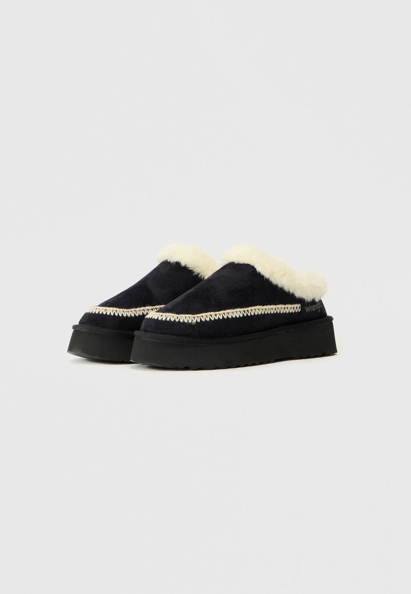 Scarpe slip-on nere con un morbido interno in shearling bianco, caratterizzate da cuciture decorative e una spessa suola in gomma nera.