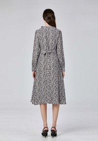 Robe à manches longues en imprimé floral noir et blanc, cintrée à la taille par un lien, jupe évasée et longueur mi-mollet. Sandales à talons noires.