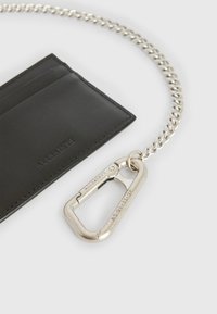 Zwart leren kaartHouser met zilveren ketting en karabijnhaak; heeft drie kaartslots, een soepele textuur en een gegraveerd logo-detail.