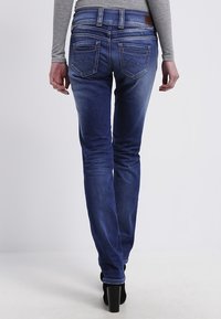 Skinny-fit blue jeans with a faded design, rear pockets featuring decorative stitching, and a leather patch on the waistband.