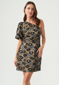 Asymmetrisk klänning i svart, guld och grått blommönster. Har en axel, texturerad tyg och en figurnära silhuett.