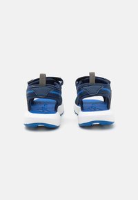 Sandales bleues avec une tige respirante, une sangle réglable, un semelle intérieure texturée et une semelle blanche rembourrée avec des accents bleus.