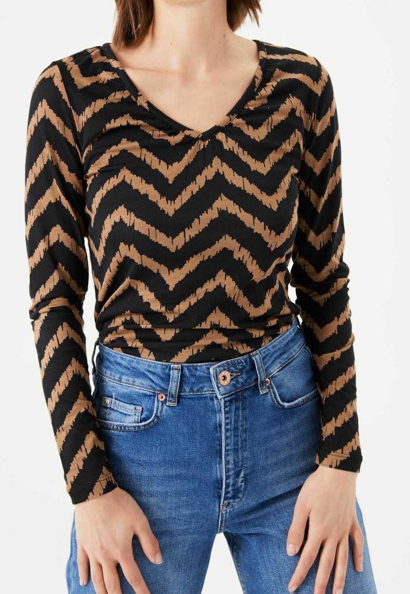Long-sleeve top in black and brown zigzag pattern, featuring a V-neckline and soft fabric, paired with blue high-waisted jeans.
