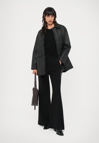 Jaqueta de couro preta sobre uma blusa de malha preta, combinada com calças largas pretas e uma bolsa escura. Sapatos de salto alto pretos com detalhes de fivela.