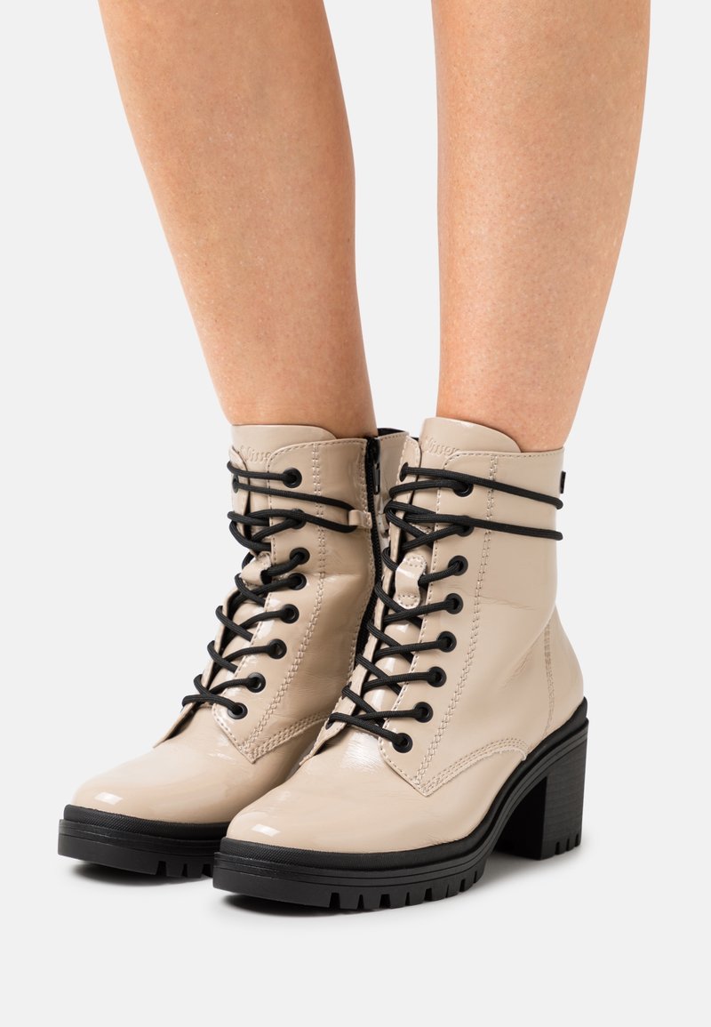 Bottines en cuir verni beige avec lacets noirs, bout arrondi et talon épais. Dotées d'une fermeture éclair latérale et d'une semelle texturée pour une meilleure adhérence.