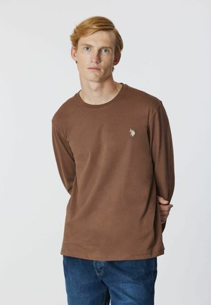 T-shirt di cotone marrone a maniche lunghe con scollatura rotonda e un piccolo logo ricamato sul petto. Sembra morbido e ha una vestibilità comoda.