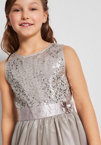 Robe à paillettes argentées avec un col rond, une ceinture en satin ornée d'une fleur, et une jupe en tulle à plusieurs couches.