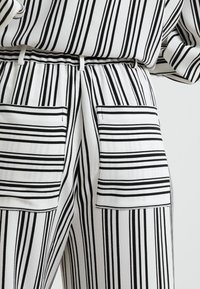 Randiga byxor i svart och vitt, med en strukturerad tygkvalitet, elastisk midja och två framfickor med horisontella ränder.