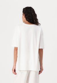 Hvit oversized T-skjorte med rund hals, korte ermer og avslappet passform. Glatt bomullsstoff, ingen synlige mønstre eller detaljer.
