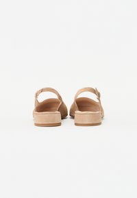 Beige suede sandals feature a block heel, an adjustable strap, and a rounded open toe design. The sole is light brown with a smooth texture.