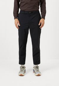 Black, lightweight pants with a drawstring waist and straight legs. Worn with beige and gray sneakers featuring blue accents.