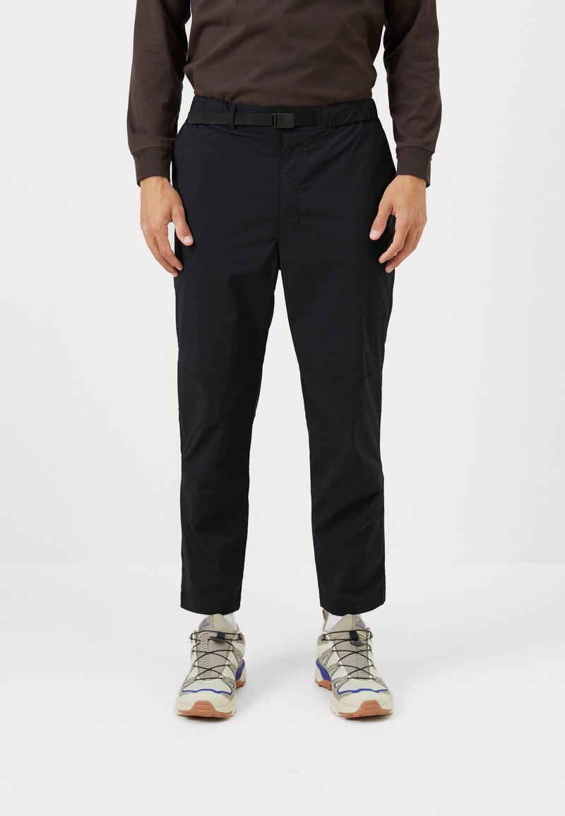 Black, lightweight pants with a drawstring waist and straight legs. Worn with beige and gray sneakers featuring blue accents.