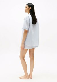 Blauw en wit gestreept shirt met korte mouwen en een losse pasvorm, gecombineerd met bijpassende shorts, gepresenteerd op een model dat blootsvoets staat.