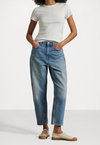 Ljusgrå t-shirt med rund halsringning i kombination med högmidjade, urtvättade blå jeans. Vita snörskor med en texturerad sula fulländar outfiten.