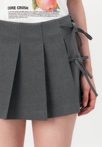 Šedá plisovaná sukně s mašlemi po stranách. Vyrobena z texturované tkaniny, s mnoha záhyby pro strukturovaný vzhled.