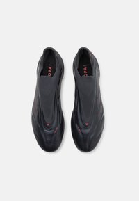 Schwarze Slipper aus glattem Leder mit Mesh-Einsätzen und roten Akzenten; abgerundete Zehenpartie und strukturierte Sohle für Grip.