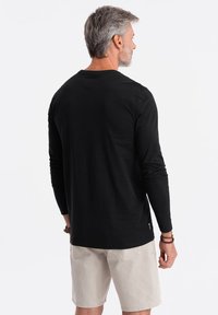 Schwarzes Langarmshirt aus Baumwolle mit rundem Ausschnitt und legerem Schnitt. Kombiniert mit hellbeigen Shorts. Einfaches Design.