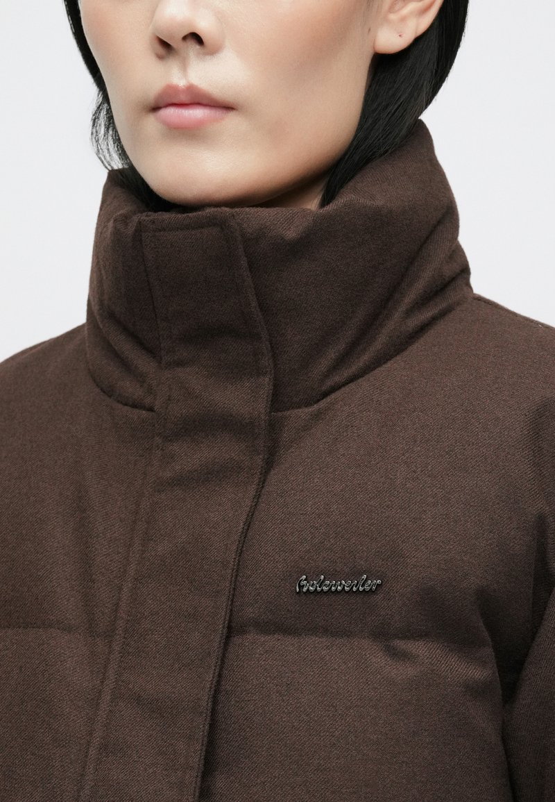 Brown high-collar jacket with a quilted texture and a small logo on the left chest. Features a structured design for warmth.