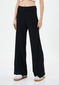 Zwarte wijde broek met een geribbelde structuur, voorzien van een elastische tailleband. Gepaard met witte sneakers, wat een casual uitstraling benadrukt.