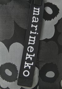 Black and gray floral patterned fabric with a woven strap featuring white "marimekko" text. Textured surface and bold shapes.