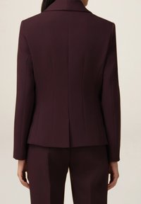 Tmavě bordó obleková bunda s klopami s výřezem, strukturálními švy a upraveným střihem. Hladká textura látky bez viditelného kovového vybavení.