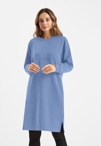 Blauwe trui jurk van zacht materiaal, met een ronde hals, lange mouwen en zijsplitten voor bewegingsgemak.
