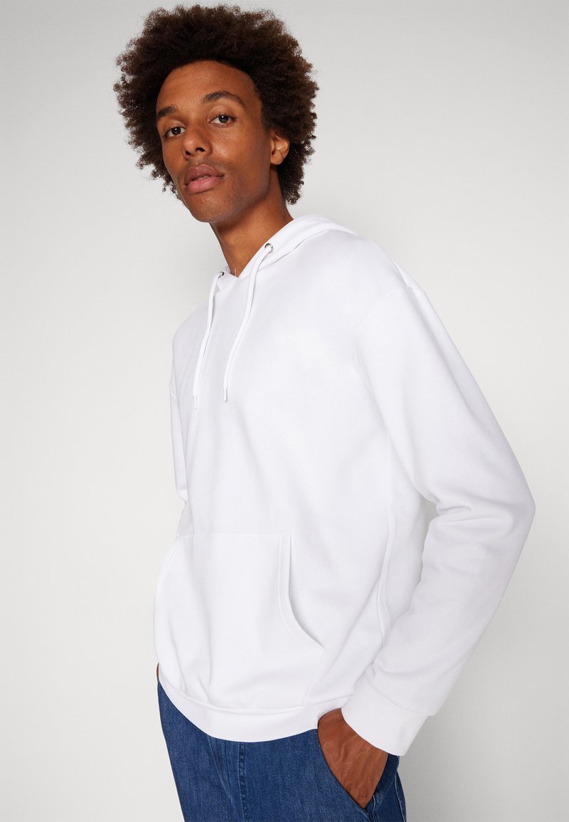 Felpa bianca con cappuccio realizzata in morbido tessuto, dotata di tasca frontale, lacci e vestibilità comoda. Abbinata a Jeans di denim blu.