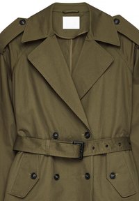 Olivgrön dubbelknäppt trenchcoat med vida slag, svarta knappar, axelklaffar och ett matchande bälte med svart spänne.