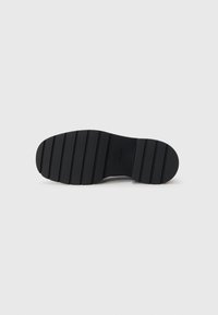 Suola di scarpa nera con scanalature orizzontali, strutturata per la presa. Presenta una punta arrotondata e una finitura liscia, marchiata con "Calvin Klein."