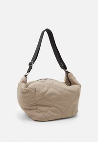 Beige gesteppte Tasche mit einer gebogenen Form, ausgestattet mit einem verstellbaren schwarzen Tragegurt und einem Reißverschluss an der Oberseite. Weiche Textur mit Rautenmuster.