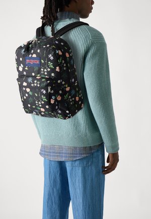 Sort rygsæk fra JanSport med blomsterprint og flere rum. Designet har lyserøde og hvide blomster på en sort baggrund.