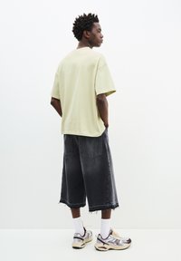 Světle zelené oversized tričko, černé denimové culottes s třepeným lemem a robustní tenisky s síťovaným detailem. Ponožky viditelné nad botou.