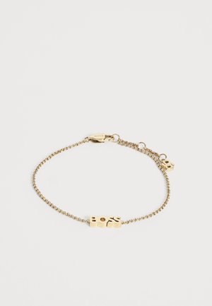 Guld kæde armbånd med rektangulær BOSS logo plade og hummerlås på en ensfarvet lys baggrund.