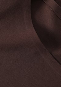 Tissu marron avec une texture lisse, affichant un léger éclat et une couleur uniforme, présentant des bords repliés sans motifs ou accents distincts.