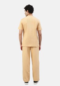 Helles beige T-Shirt mit kurzen Ärmeln, kombiniert mit passenden Hosen, die einen lässigen Schnitt und ein weiches Material aufweisen. Einfaches Design, ohne sichtbare Muster.