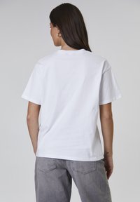 Witte katoenen t-shirt met een relaxed fit, korte mouwen en een ronde hals, gecombineerd met grijze denim jeans met achterzakken.